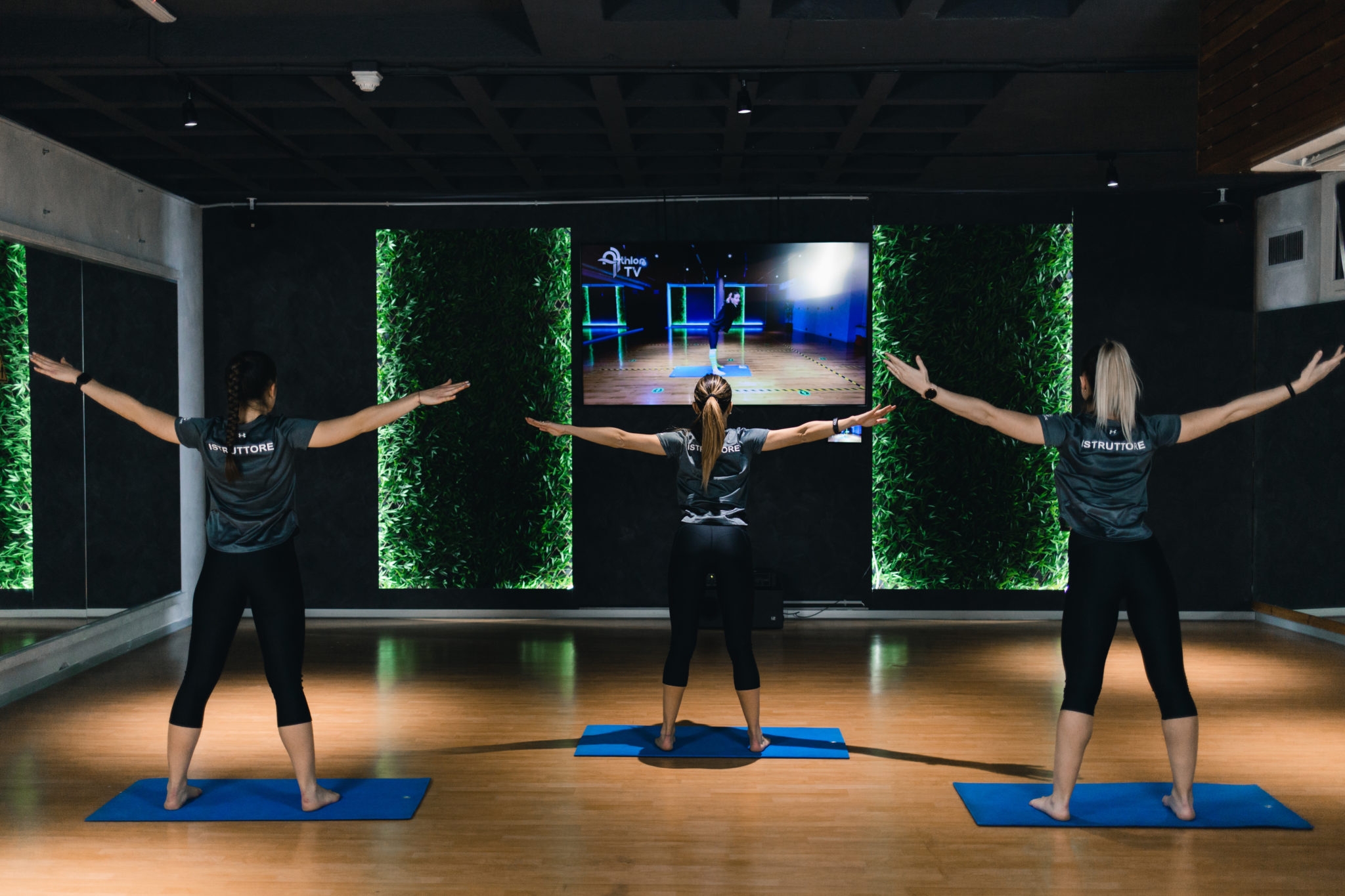 tres mujeres vestidas de negro en el gimnasio haciendo ejercicio frente al televisor